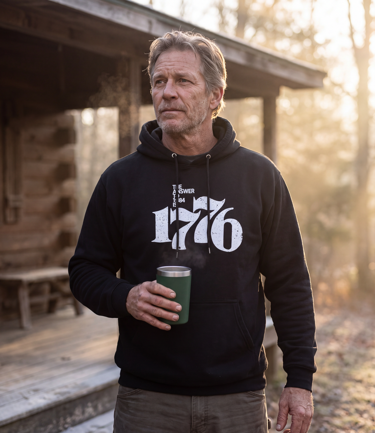 Man wearing The Answer To 1984 Is 1776 Hoodie in black at a cabin porch at dawn