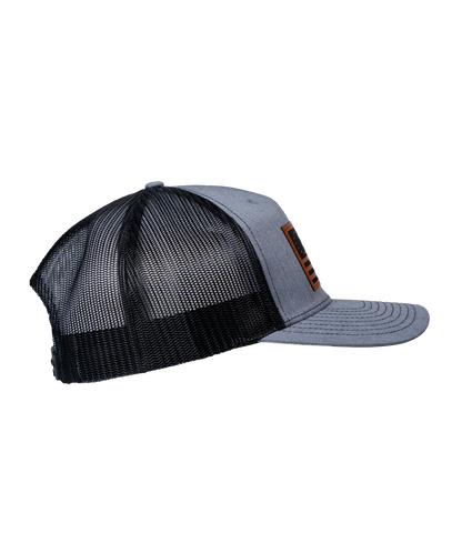 The Alex Jones Store - Heather grey and black trucker hat, right side view, featuring leather American flag patch on the front panel