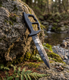 The Alex Jones Store - Outdoor lifestyle photo of Liberty or Death Trench War Dagger resting on mossy rock by a creek, etched blade visible