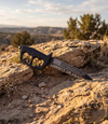 The Alex Jones Store - Liberty or Death Trench War Dagger leaning on desert rock at golden hour, American flag and slogan etched on blade
