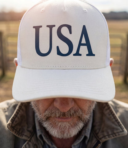The Alex Jones Store - Older bearded man wearing white 'USA' Premium Trucker Hat with navy serif USA print, close-up rural backdrop